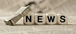 Wooden blocks spelling “News” beside a small newspaper on a desk