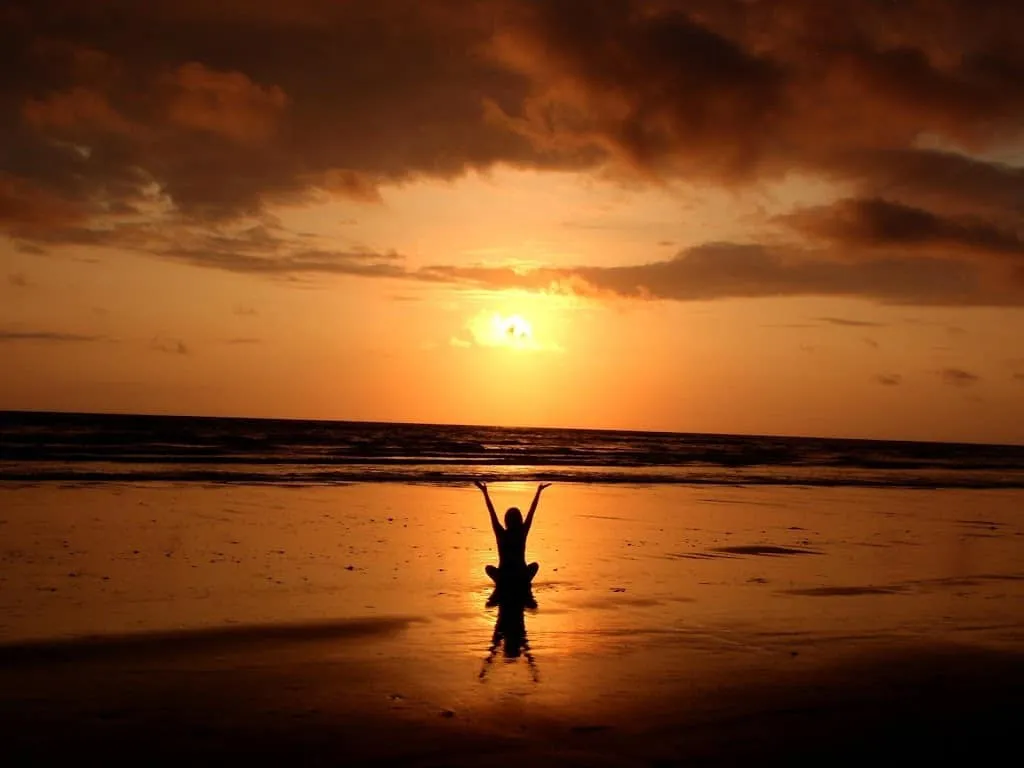 Silhouette on a beach raising arms toward a glowing sunset over the ocean