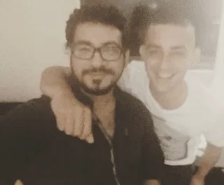 Two men posing for a low-resolution selfie, one with glasses and the other smiling with an arm around him