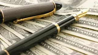 Fountain pen resting on dollar bills, suggesting earning money from writing