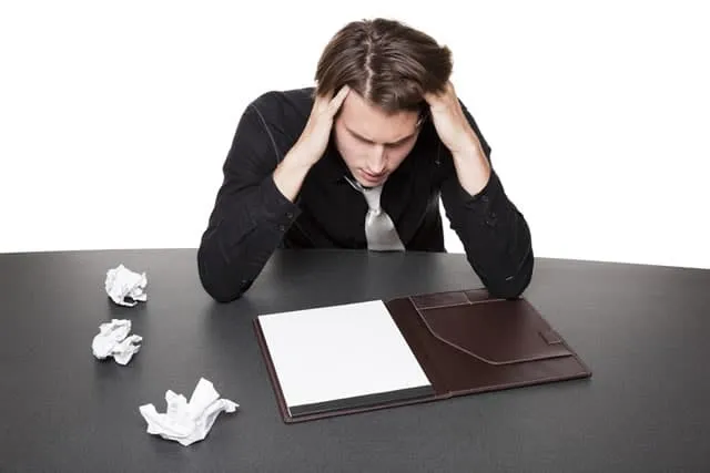 Frustrated writer staring at a blank page with crumpled paper nearby